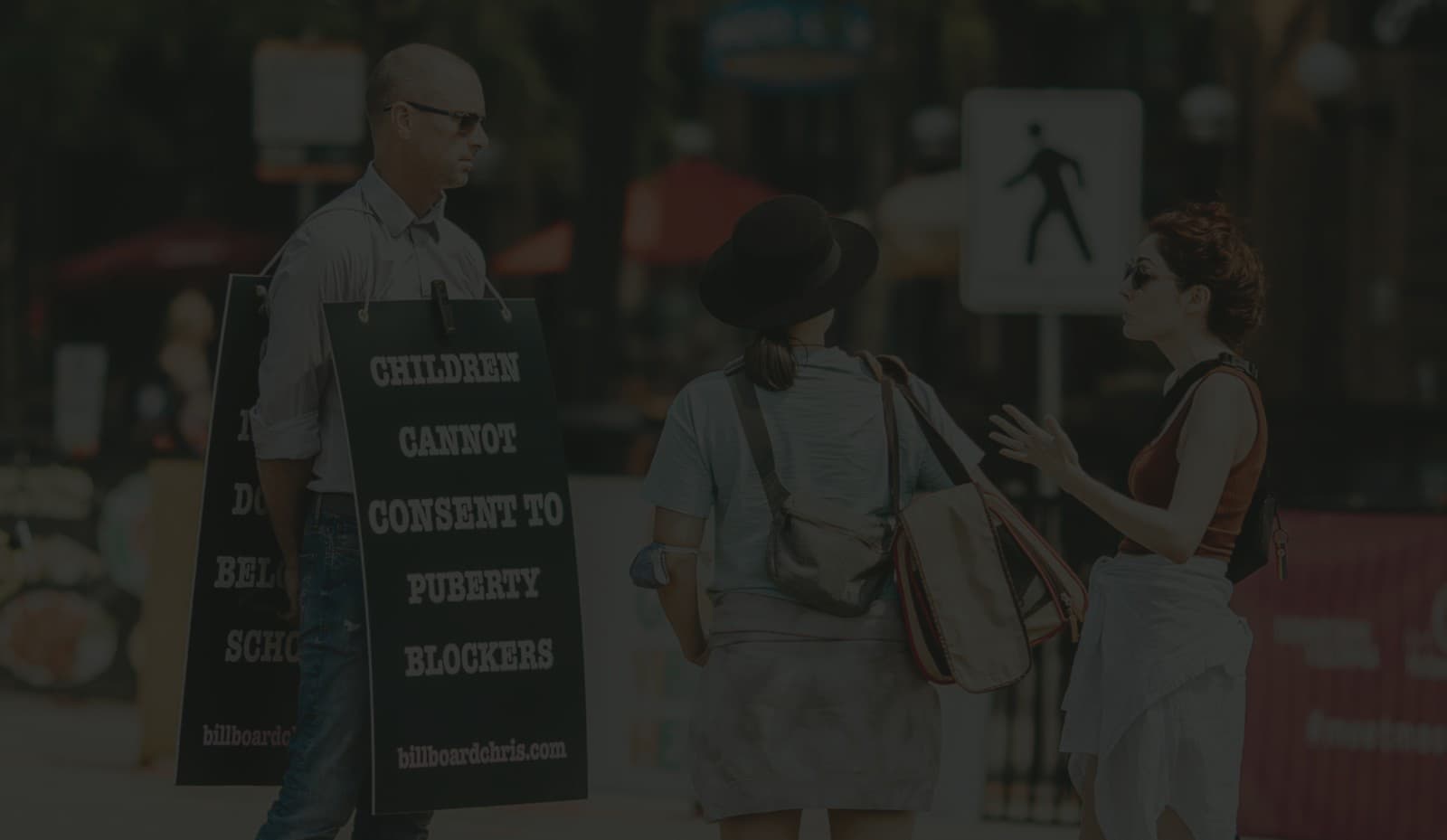 Billboard Chris habla en una acera pública con un cartel que dice que los niños no pueden consentir los bloqueadores de la pubertad